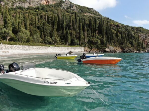 This is an image of Kardamili Boat Rental boats, in Kalamitsi Beach Mani. The sea is blue and green and the background is full of trees.