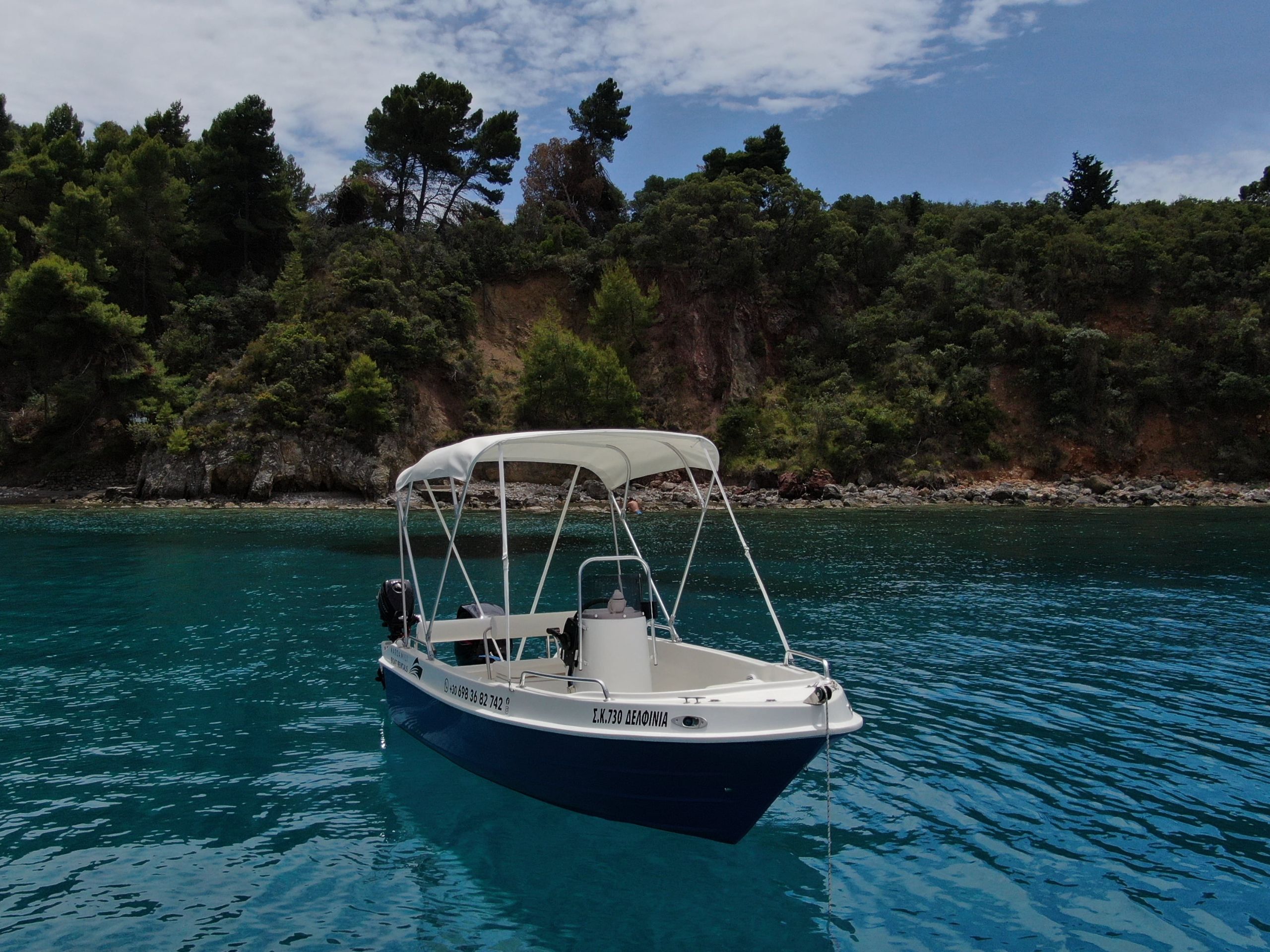 This is an image of our Kardamili Boat Rentals Delfinia Boat in Mani, with a coast full of trees at the background.