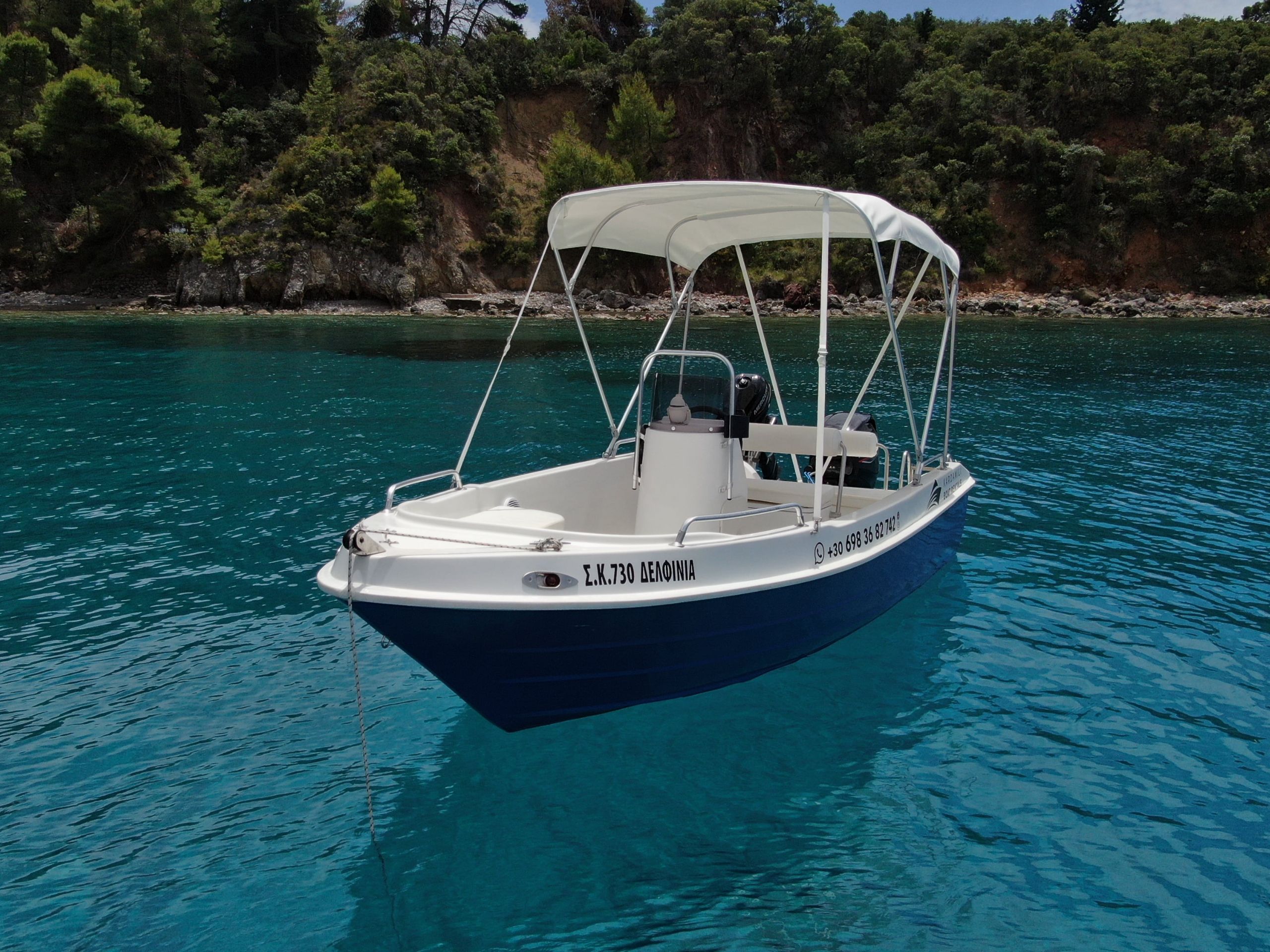 This is an image of our Kardamili Boat Rentals Delfinia Boat in Mani, with a coast full of trees at the background.