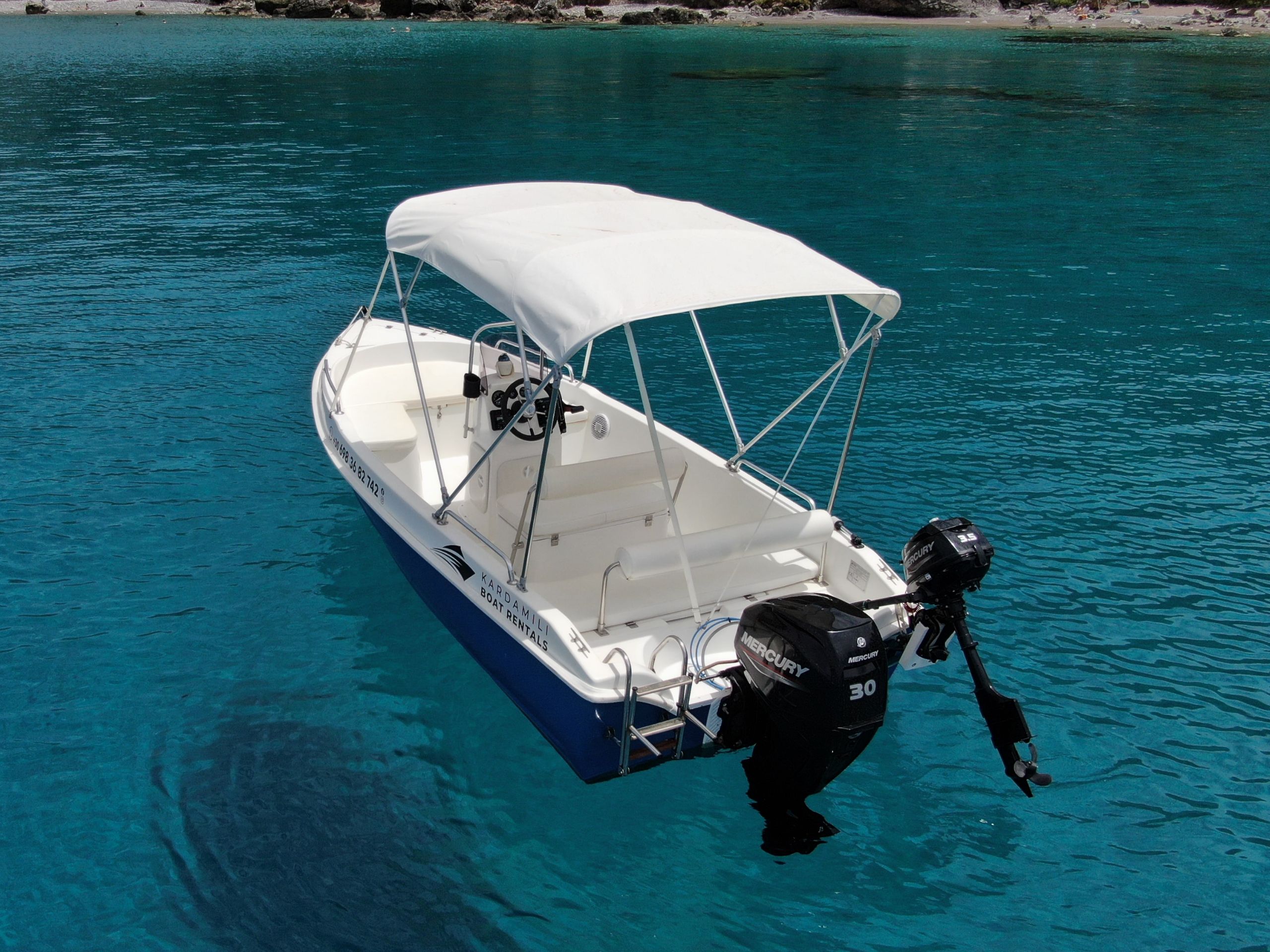 This is an image of our Kardamili Boat Rentals Delfinia Boat in Mani, with a coast full of trees at the background.