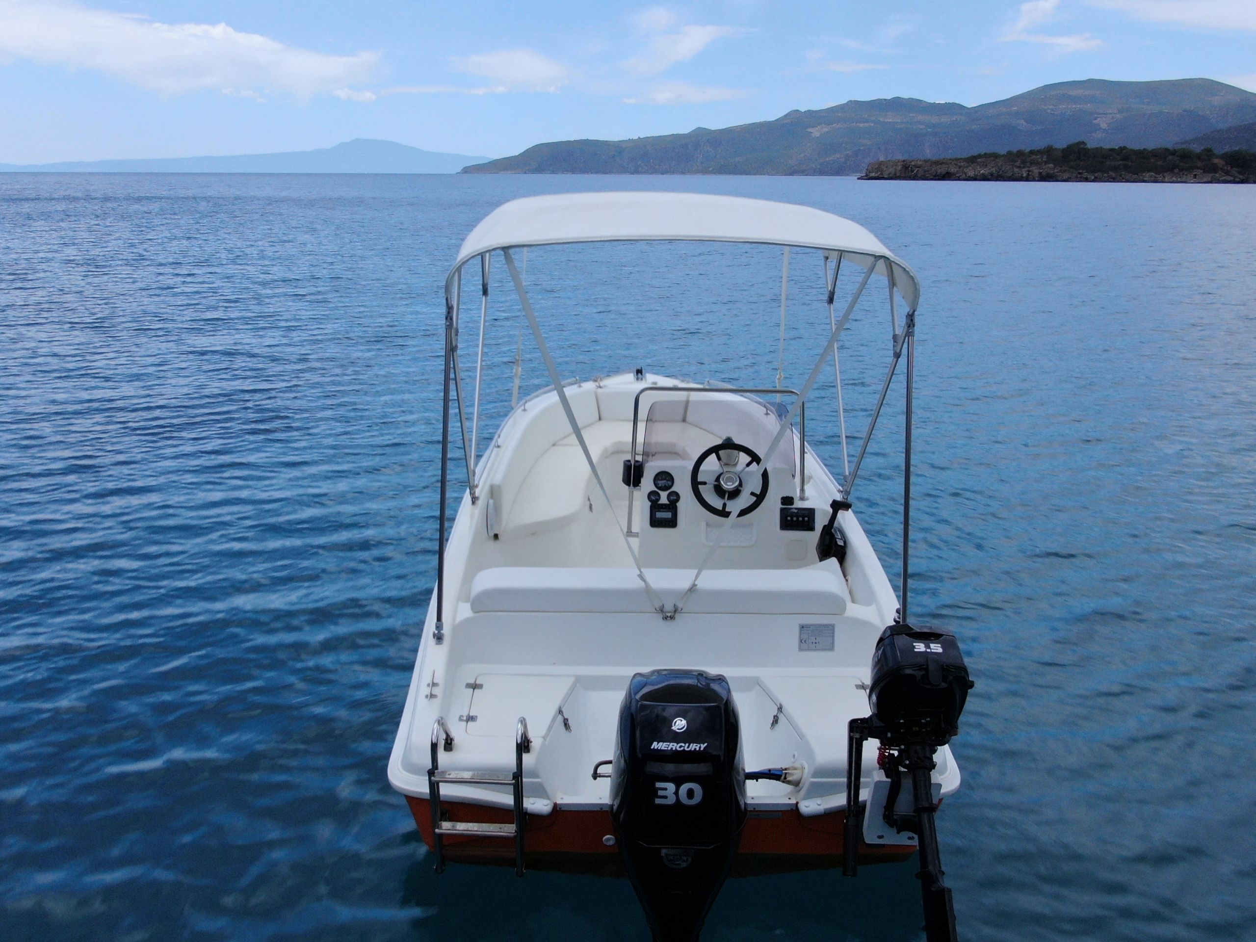 This is an image of our orange Kardamili Boat Rentals Boat, called Kalogria, at the Mani sea. At the background there is a coast with trees and rocks.