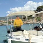 This is an image of Vasilis Tatsis, one of our members. He's at Kardamili Harbor at the Green Boat, smiling and wearing a yellow Kardamili Boat Rentals sweater. He's also wearing a hat.